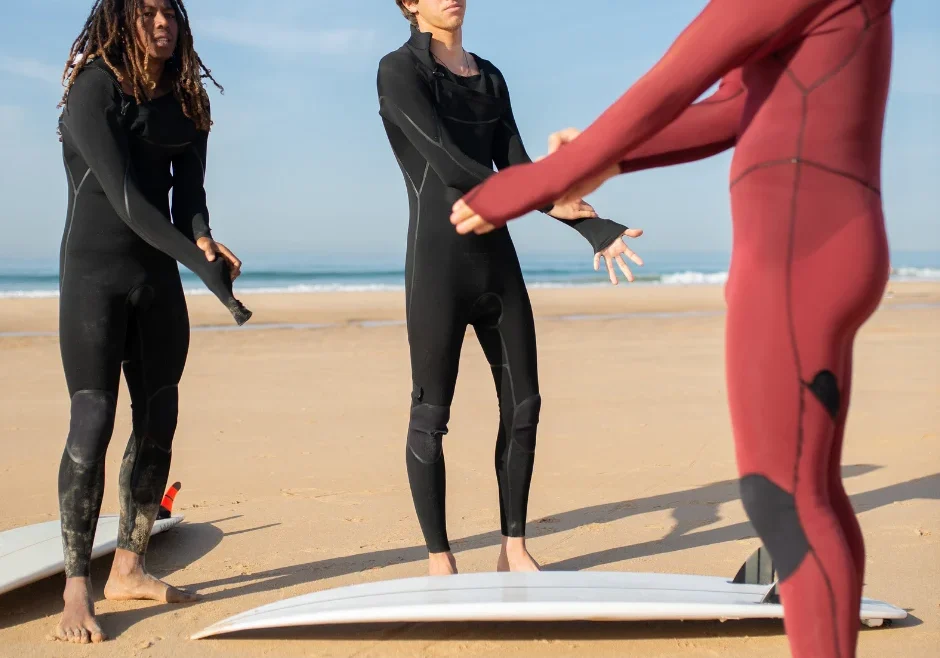3 chicos con diferentes tipos de trajes de neopreno preparándose para hacer surf
